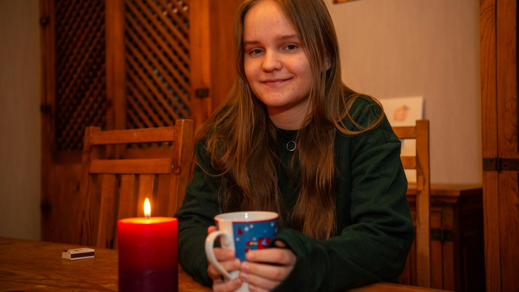 Kira Grohs sitzt mit einer Weihnachtstasse in den Händen am Esstisch ihrer Eltern, vor ihr brennt eine Kerze.