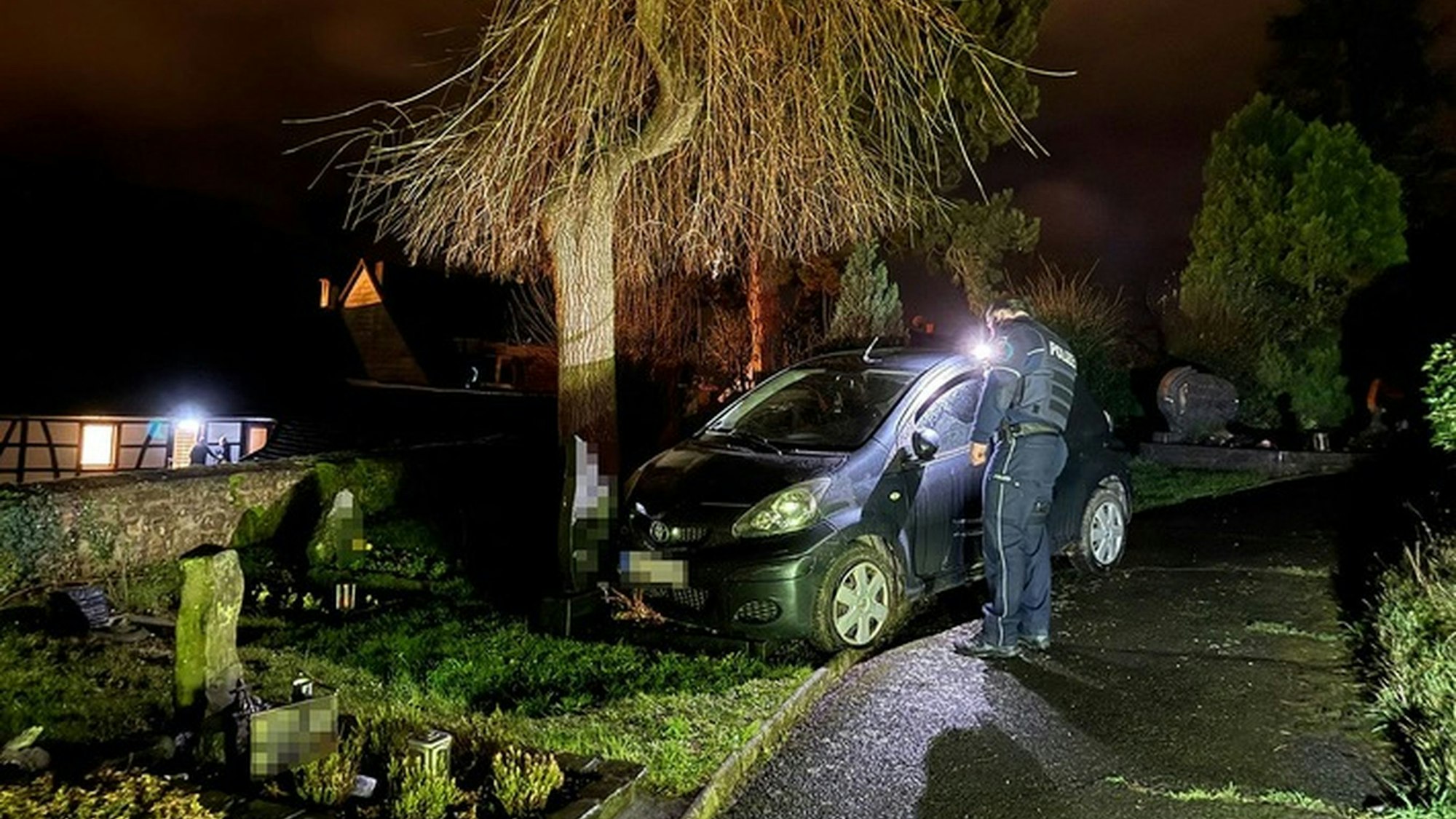 Ein Auto steht nachts auf einem Friedhof, ein Polizist daneben.