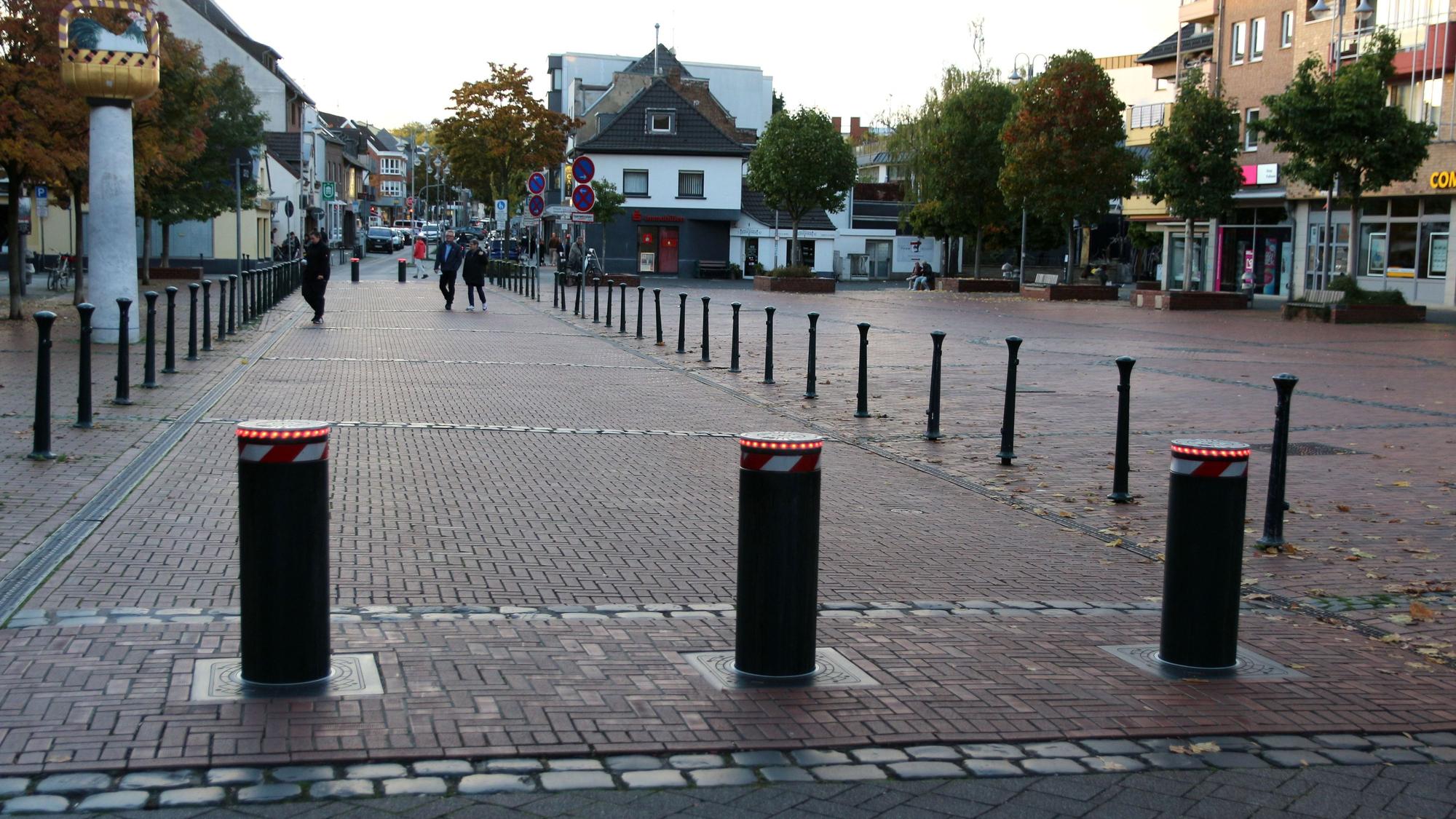 Drei versenkbare Poller, im Hintergrund ein Marktplatz und ein paar Passanten.