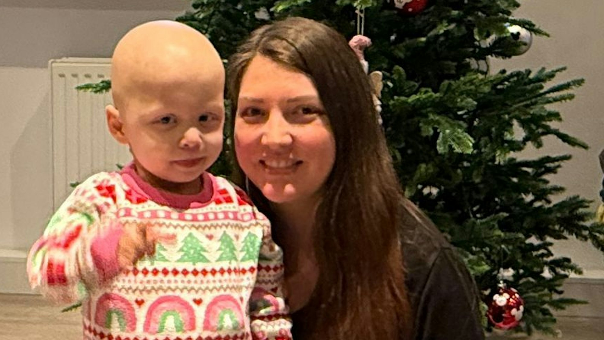 Das Foto zeigt die kleine Juna mit ihrer Mutter vor einem Weihnachtsbaum.