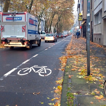 Autos und Lkw fahren auf der Vorgebirgstraße in Zollstock. Rechts vor dem Gehweg wird ein Fahrradschutzstreifen eingerichtet.
