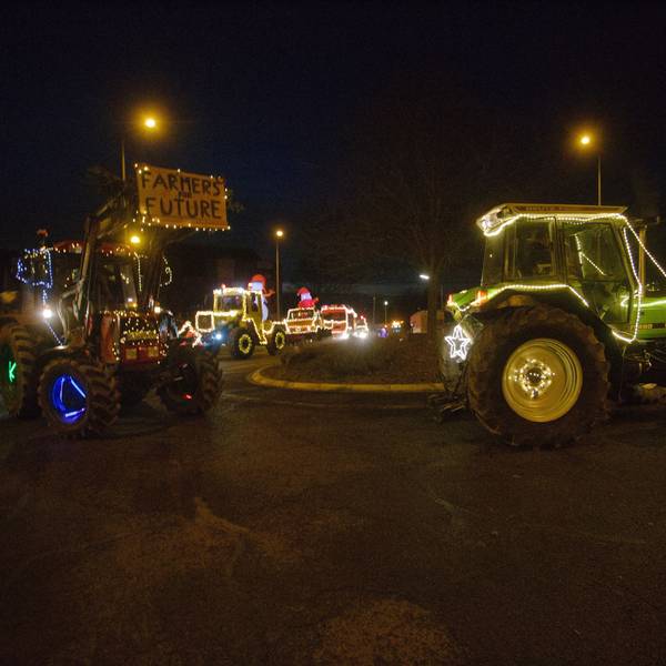 Mit bunten Lichtern geschmückte Traktoren fahren durch einen Kreisverkehr bei Nacht.