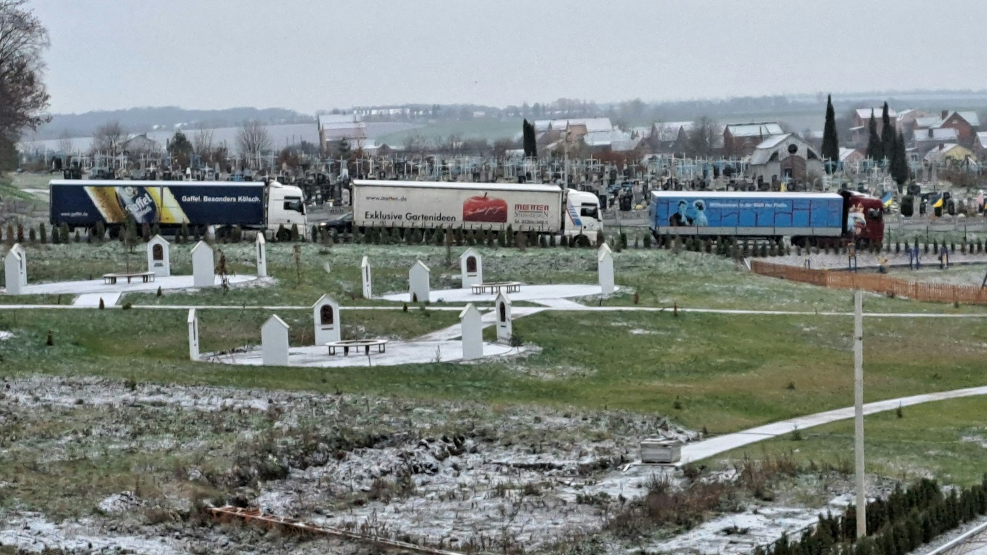 Drei Lastzüge der Humanitären Hilfe Overath stehen an einem Friedhof im südukrainischen Chmelnyzkyj.