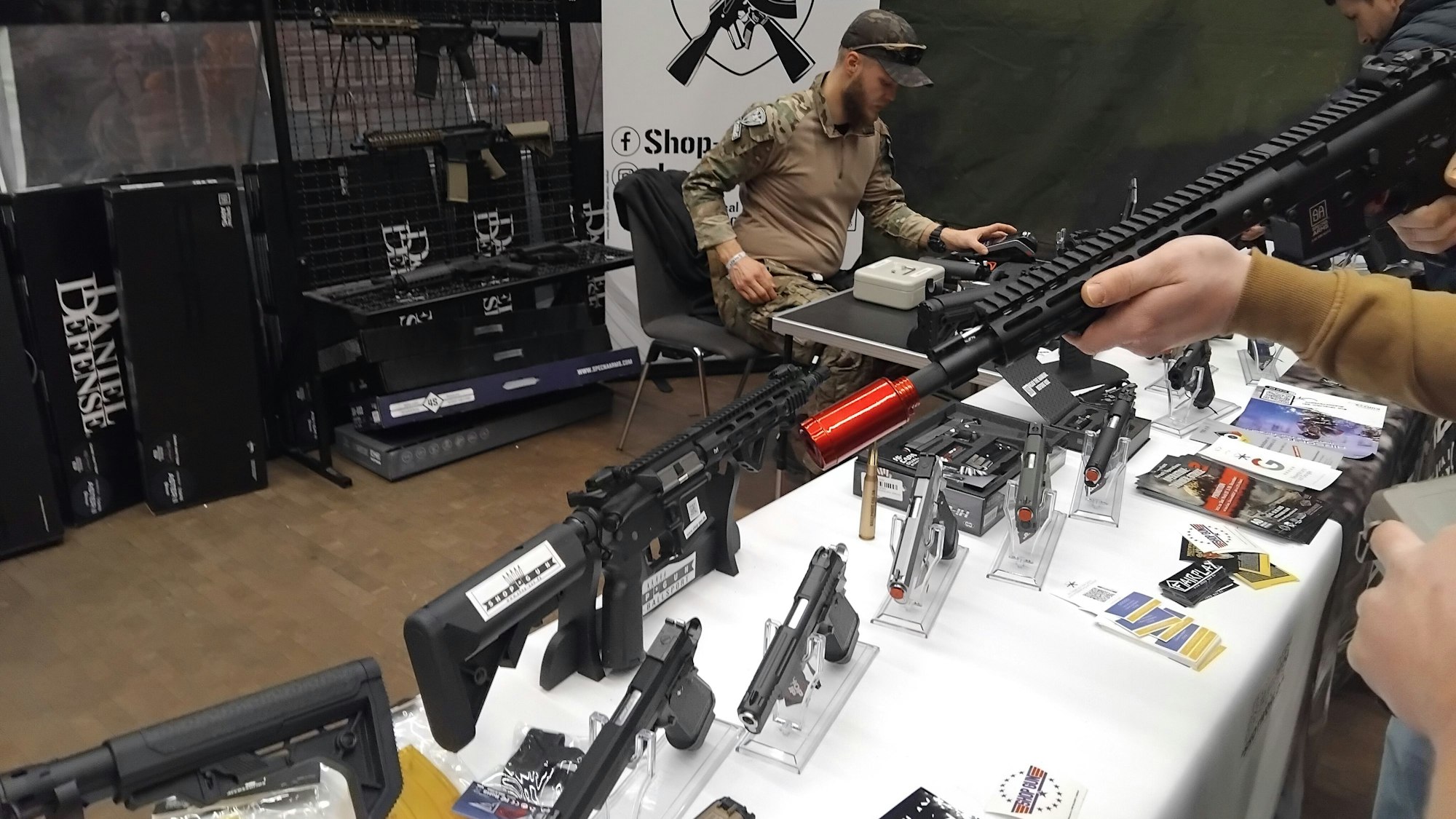 Mehrere Pistolen stehen aufgereiht auf einem Tisch, ein Kunde hält ein großes Modell in der Hand.