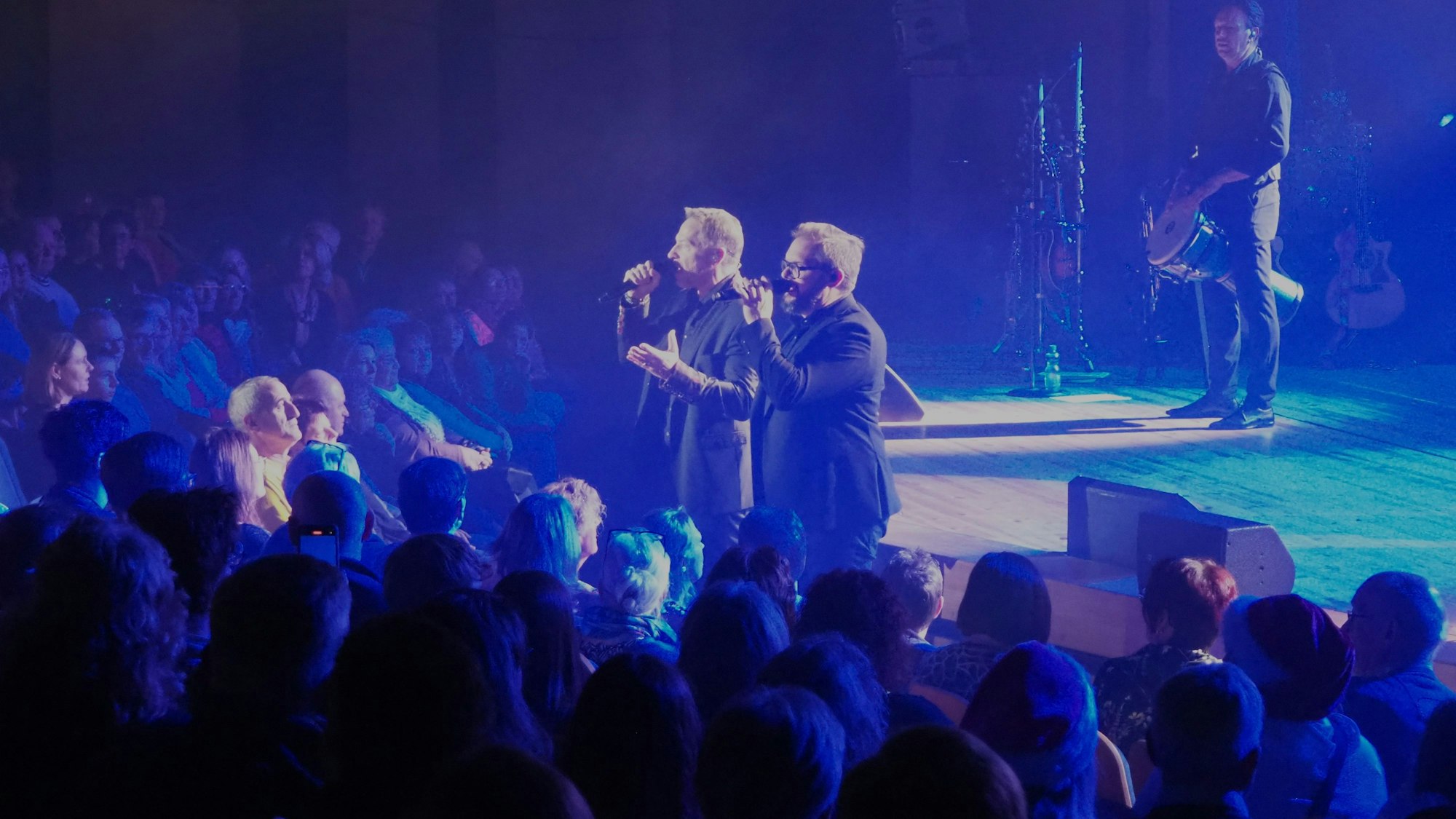 Zwei Höhner-Sänger stehen in blaues Licht getaucht vor Publikum.
