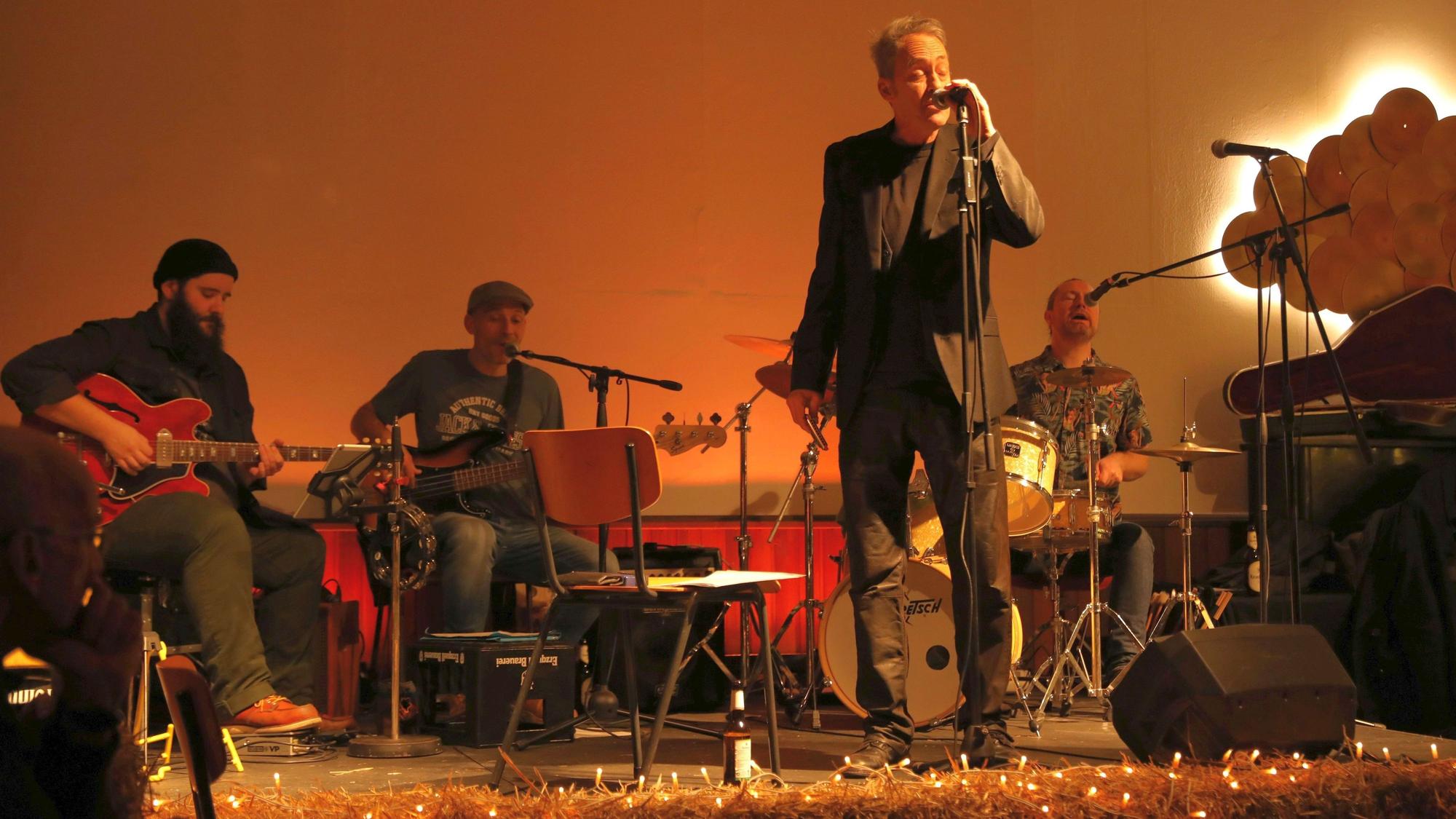 Ein Sänger am Mikrofon, dahinter drei sitzende Musiker.