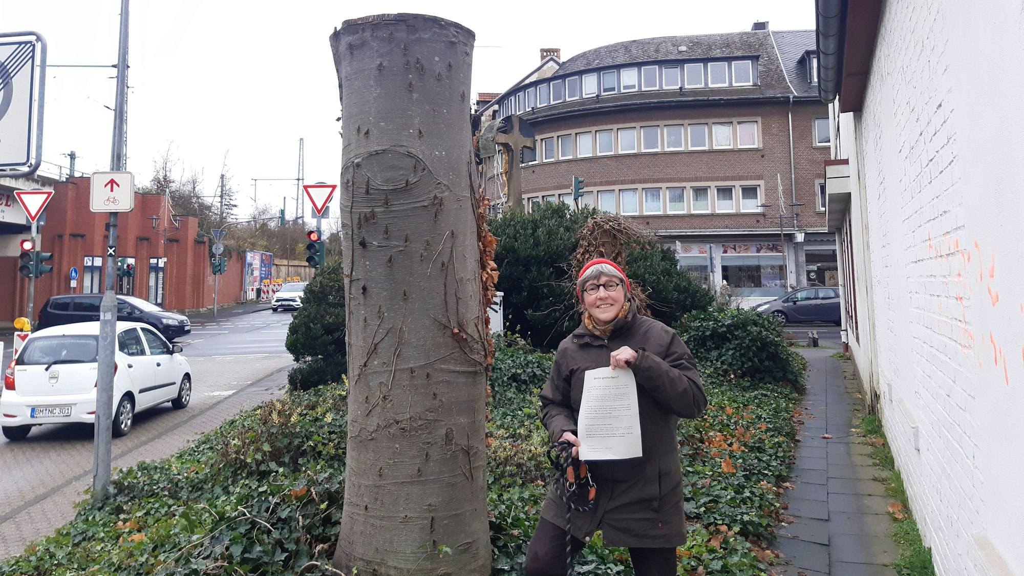 Das Foto zeigt Elke Bader mit einem Flugblatt in der Hand neben dem Stamm der abgeholzten Blutbuche.