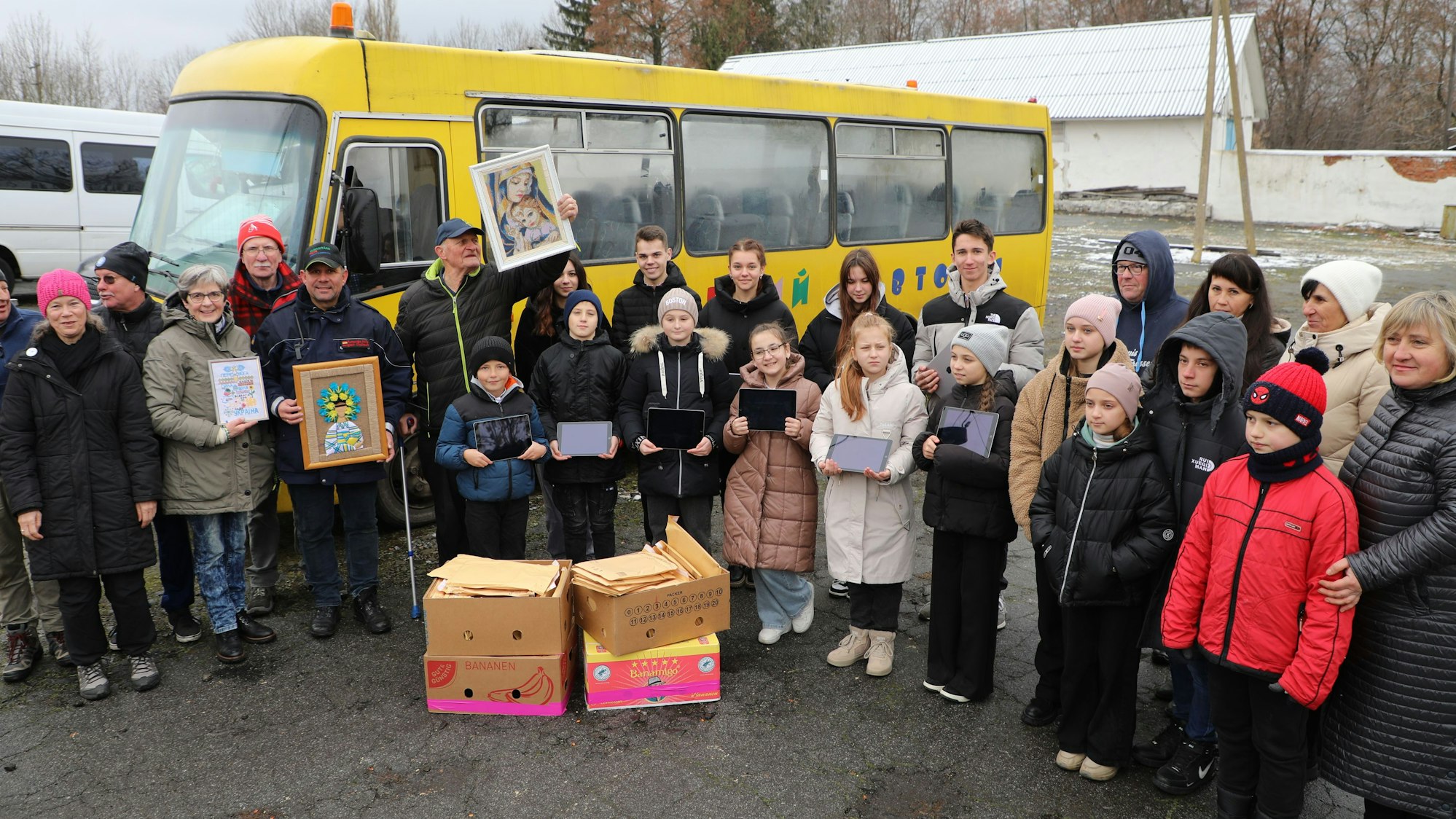 Schülerinnen und Schüler eine Schule im südukrainischen Chmelnyzkyj stehen mit Tabletts in den Händen singend vor ihrem Schulbus.