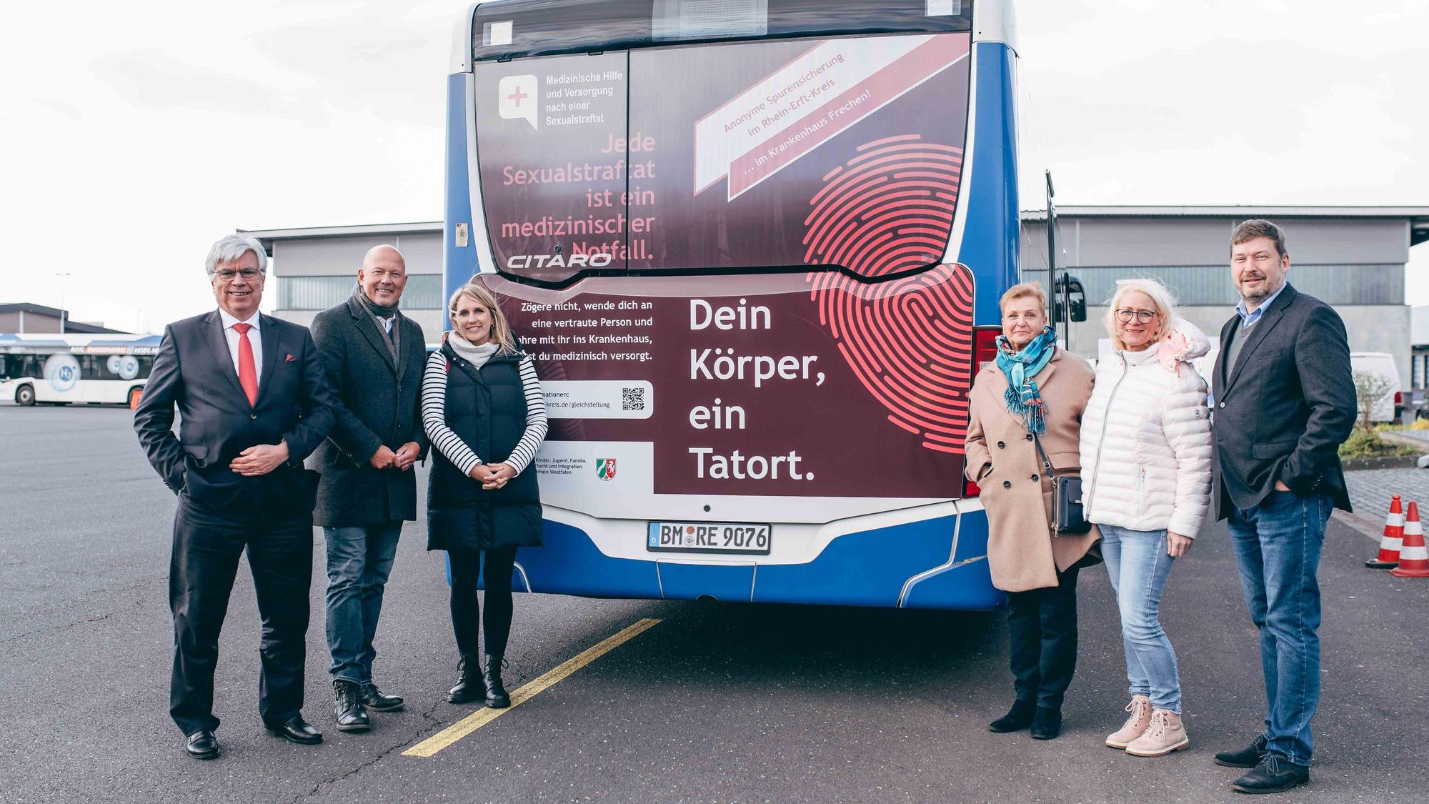 Auf dem Foto ist ein Linienbus zu sehen, vor dem mehrere Frauen und Männer stehen.