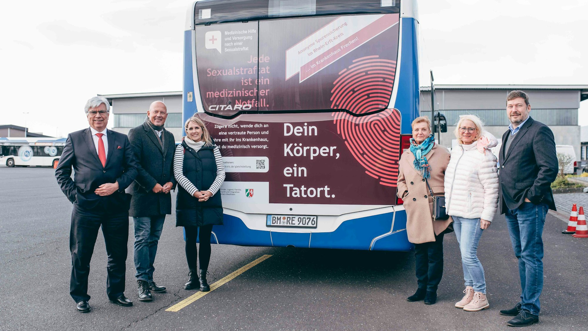 Auf dem Foto ist ein Linienbus zu sehen, vor dem mehrere Frauen und Männer stehen.
