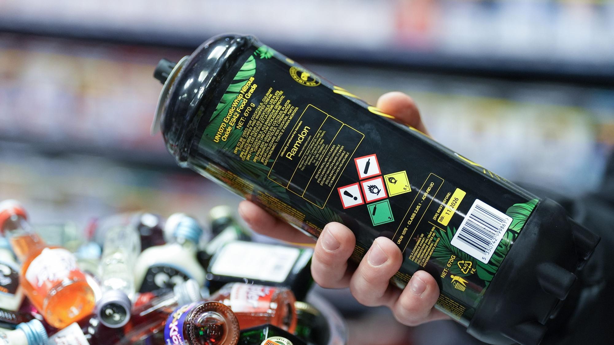 Ein Mitarbeiter hält eine Dose Lachgas am Tresen eines Kiosks in der Hand.