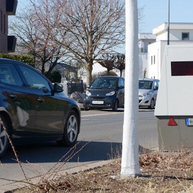 Das Bild zeigt die Messanlage, auf der Straße fährt ein Auto. Im Hintergrund stehen weitere Wagen.