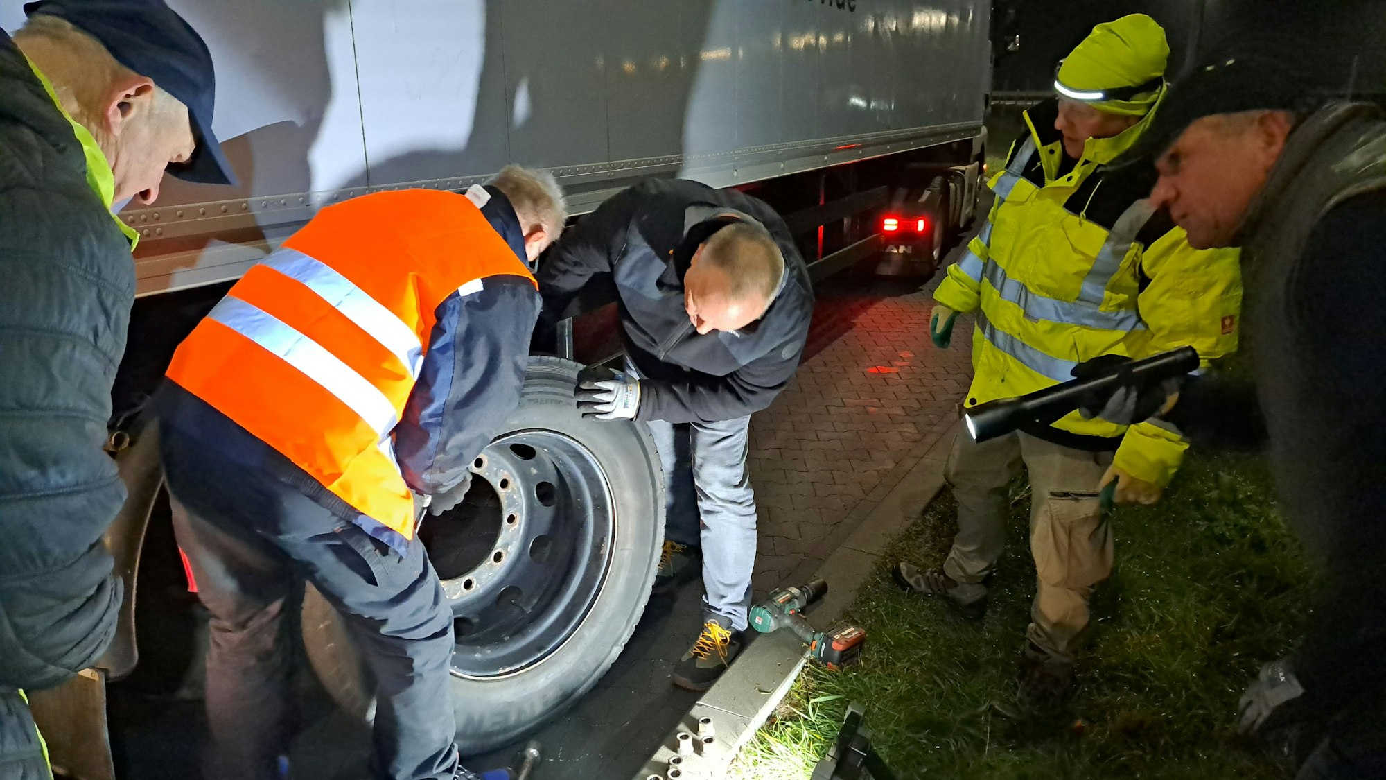 Männer wechseln in der Nacht ein Rad an einem Lkw-Auflieger.