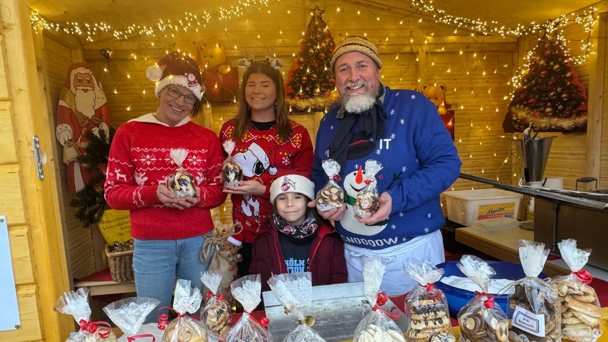Zwei Frauen, ein Mann und ein Kind tragen Nikolausmützen und halten Tüten mit Weihnachtsgebäck in Händen.