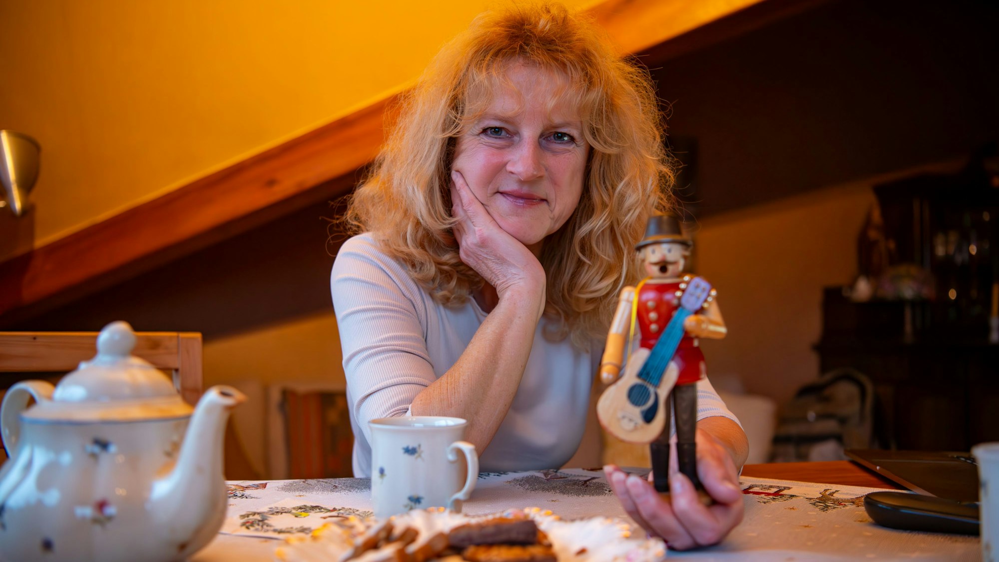 Katia Franke sitzt mit einem Räuchermännchen in der Hand an einem Tisch. Vor ihr stehen ein Teller mit Plätzchen, eine Teekanne und eine Tasse.