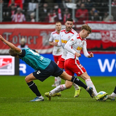 08.12.2024, Bayern, Regensburg: Fußball: 2. Bundesliga, Jahn Regensburg - 1. FC Köln, 15. Spieltag, Jahnstadion Regensburg. Timo Hübers von Köln (l-r), Dominik Kother von Regensburg und Jan Thielmann von Köln kämpfen um den Ball. Foto: Armin Weigel/dpa - WICHTIGER HINWEIS: Gemäß den Vorgaben der DFL Deutsche Fußball Liga bzw. des DFB Deutscher Fußball-Bund ist es untersagt, in dem Stadion und/oder vom Spiel angefertigte Fotoaufnahmen in Form von Sequenzbildern und/oder videoähnlichen Fotostrecken zu verwerten bzw. verwerten zu lassen. +++ dpa-Bildfunk +++