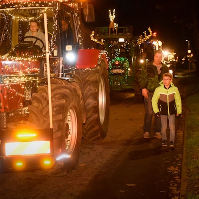 Auf dem Foto sind mit Lichterketten geschmückte Traktoren zu sehen. Menschen stehen am Wegesrand und verfolgen den Zug.