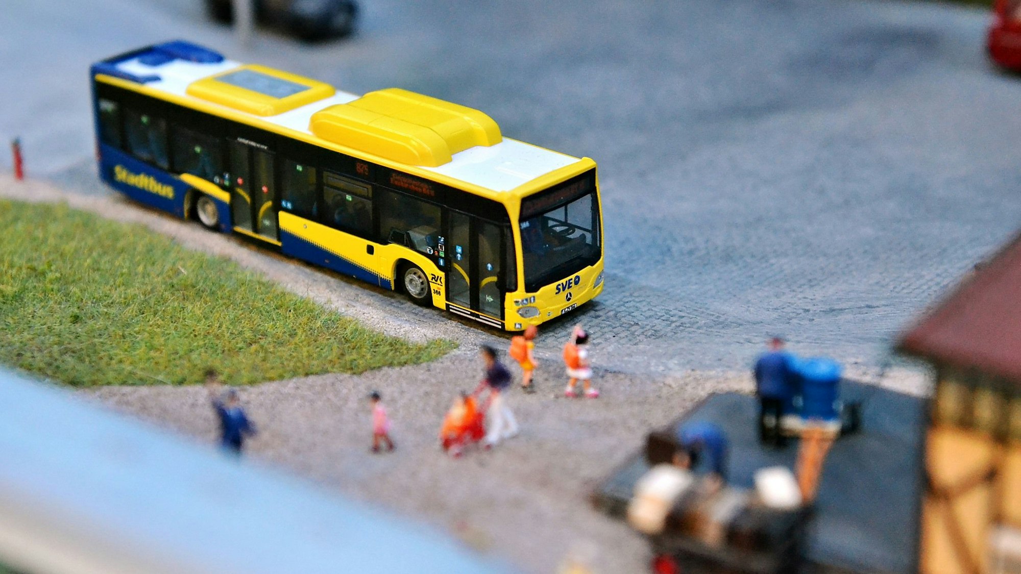 Ein gelber Miniaturbus steht in einer Modelllandschaft.