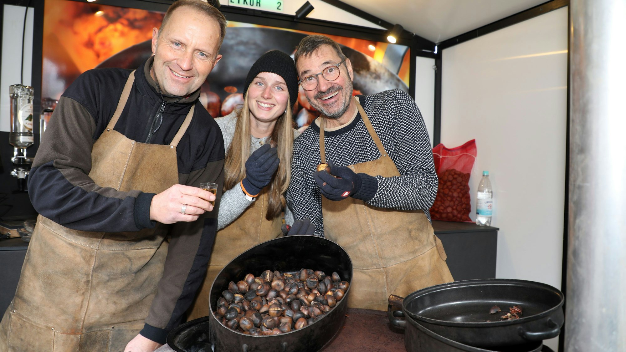 Drei Menschen stehen hinter einem Topf mit Maronen auf einem Herd
