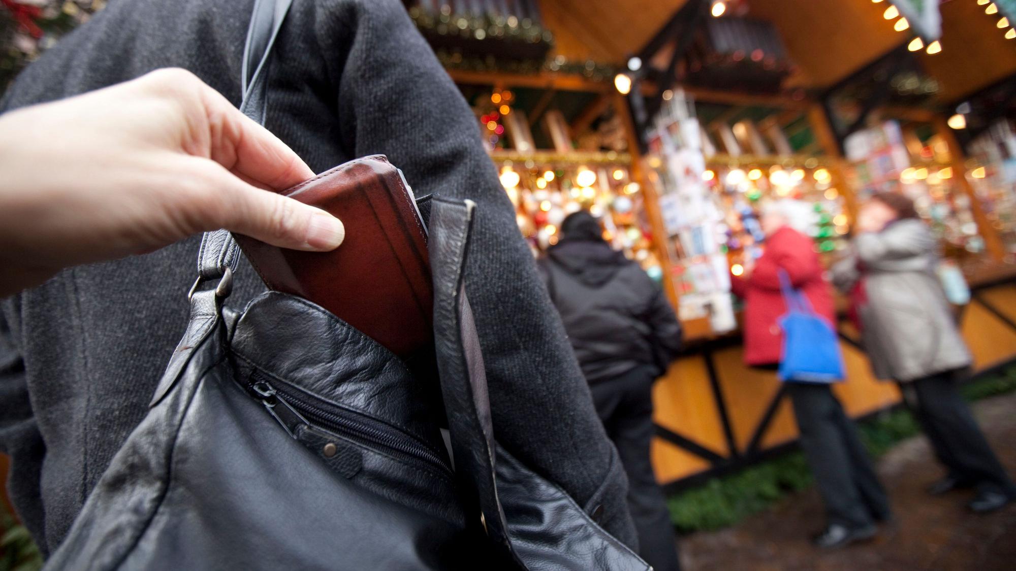 Das Foto zeigt eine Hand, die ein Portemonnaie aus der Handtasche einer Person herauszieht.