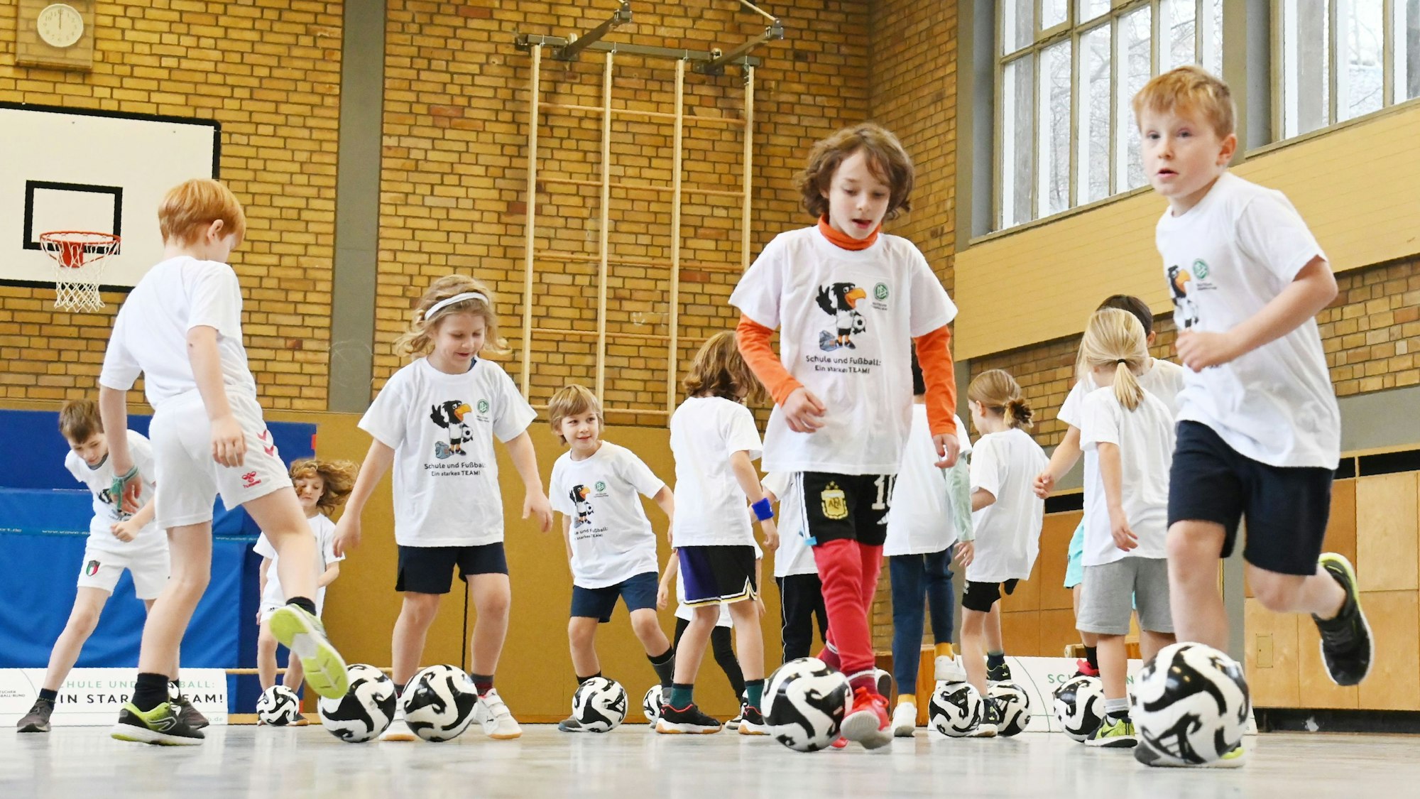 Kinder spielen in einer Turnhalle mit Fußbällen.