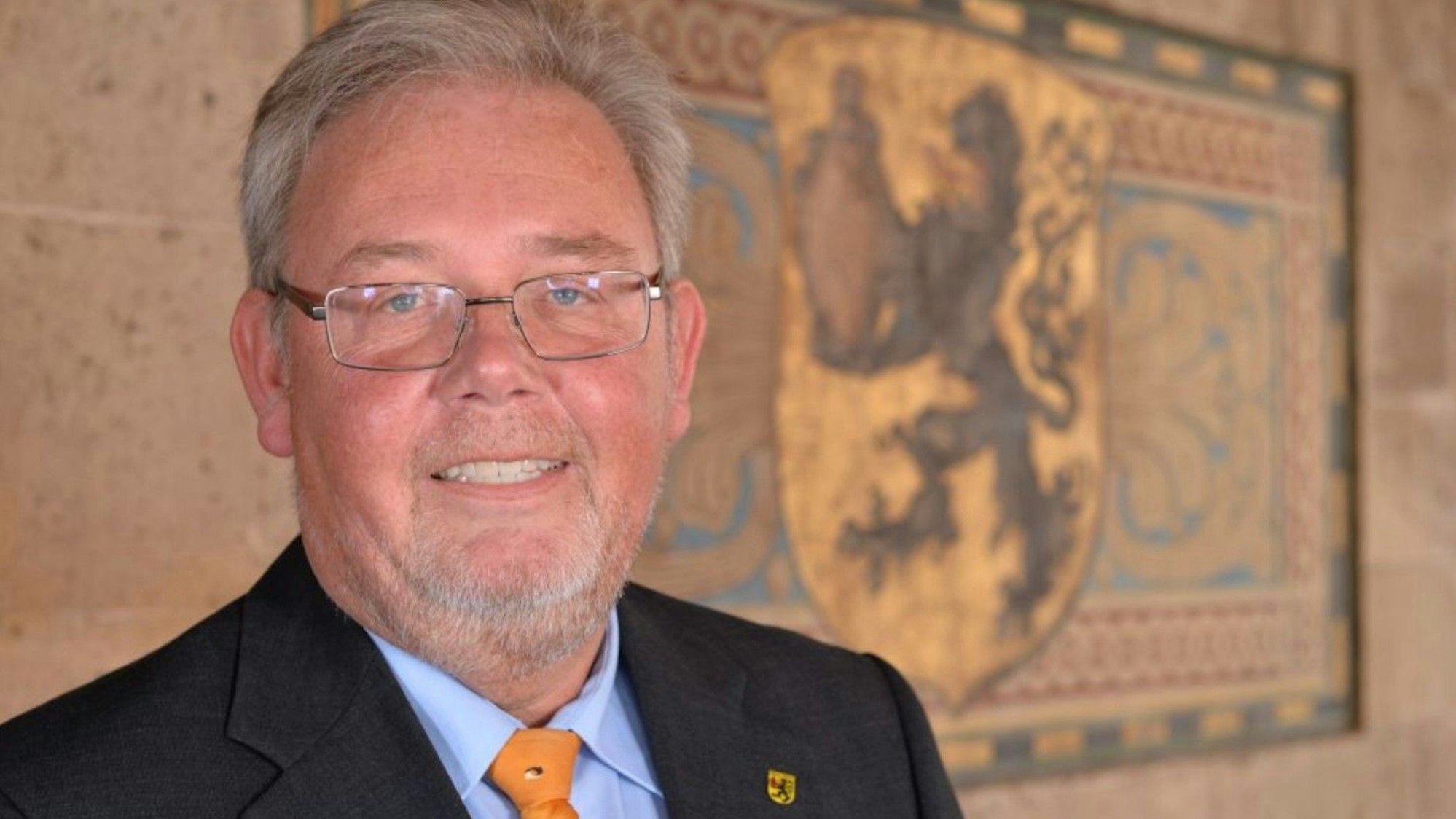 Auf dem Bild ist ein Politiker vor dem Stadtwappen zu sehen.