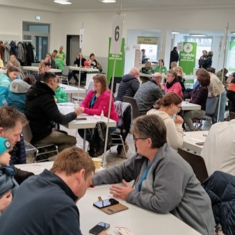 Menschen aller Altersklassen sitzen an Tischen und lassen sich das Prozedere erklären.