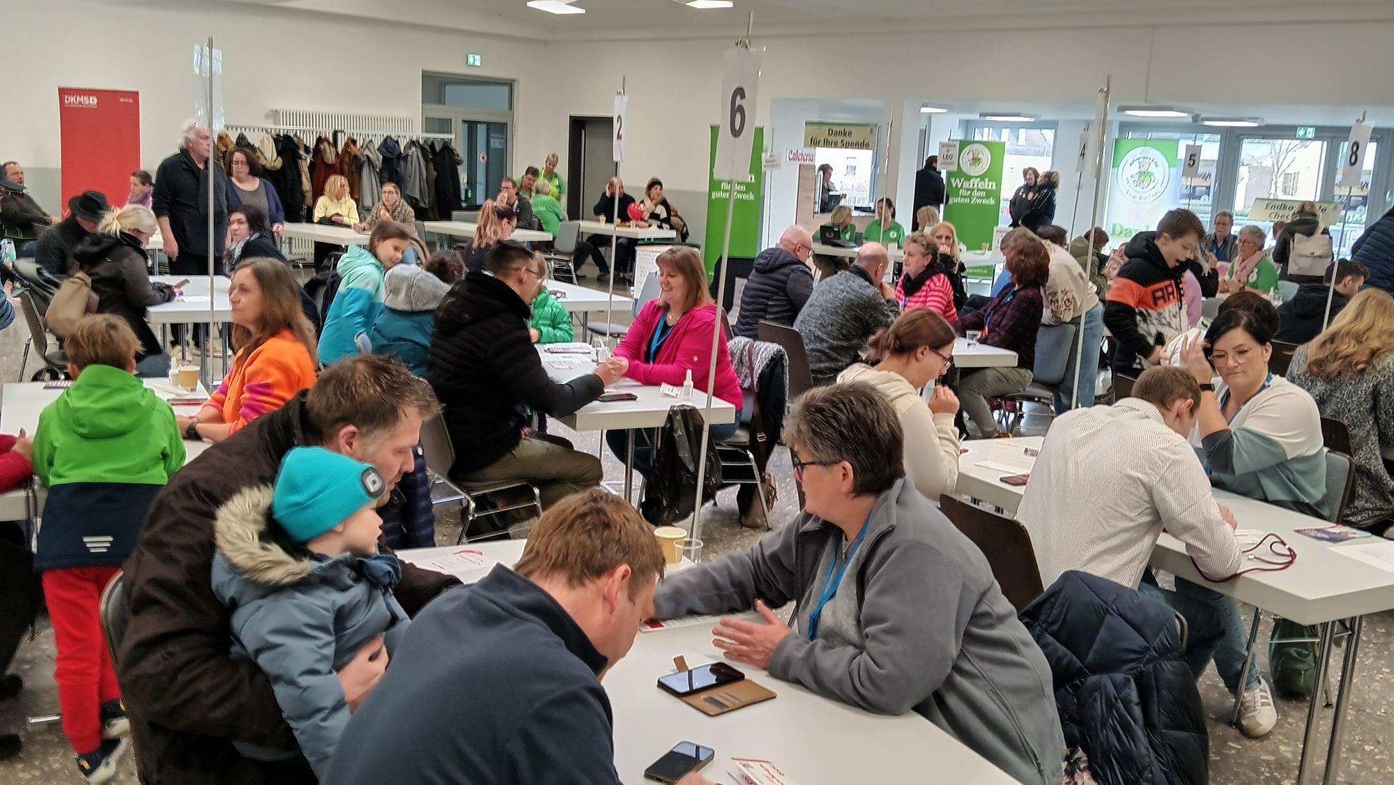 Viele Menschen sitzen in einem großen Raum an Tischen.