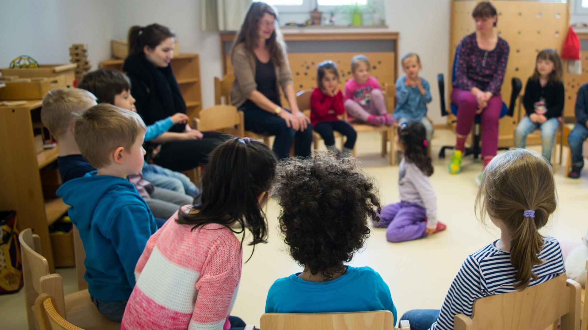 Kinder und Erzieherinnen sitzen in einer Kindertagesstätte in Düsseldorf (Nordrhein-Westfalen) im Kreis.