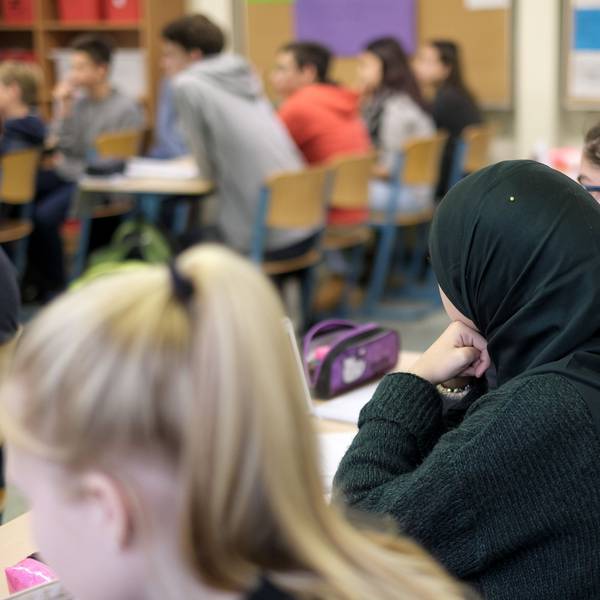 Ein Schülerin mit Kopftuch sitzt zischen ihren Mitschülern.