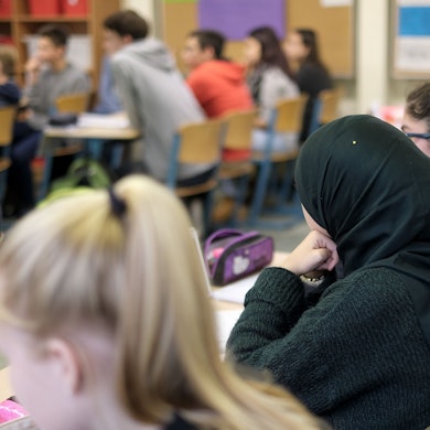 Ein Schülerin mit Kopftuch sitzt zischen ihren Mitschülern.