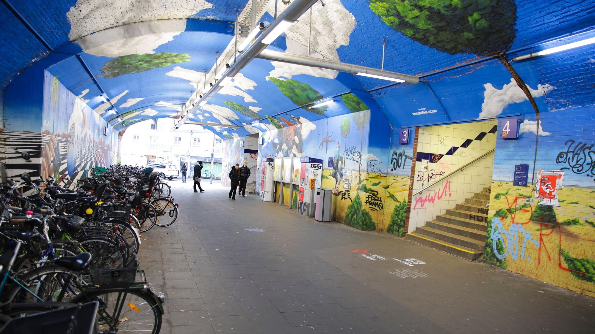 Eine Unterführung mit Bildern an den Wänden. Fahrräder stehen in einer Ecke.