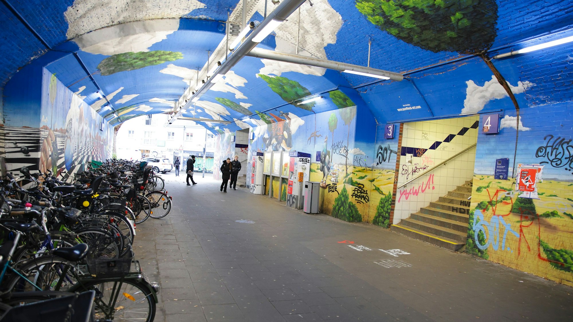 Eine Unterführung mit Bildern an den Wänden. Fahrräder stehen in einer Ecke.