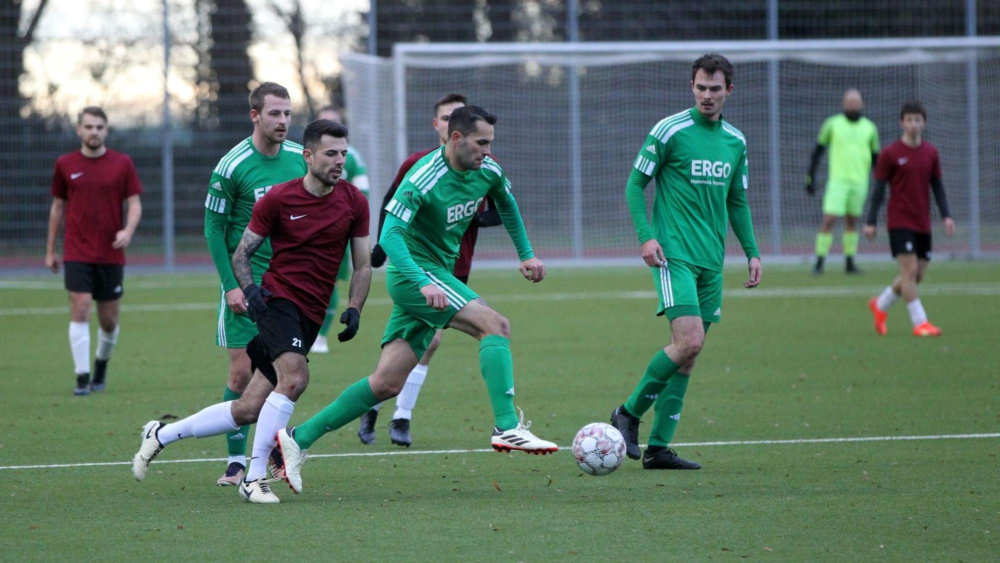 Ein Fußballer läuft mit dem Ball am Fuß. Mitspieler und Gegenspieler schauen ihm zu.