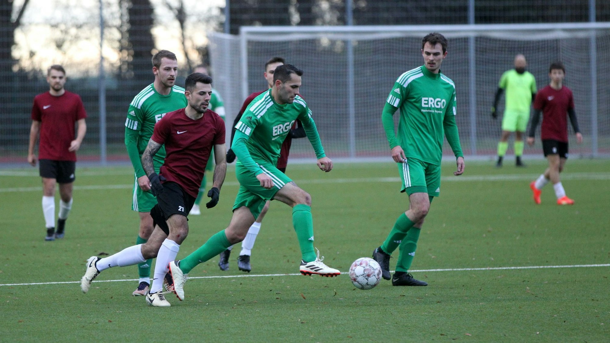 Ein Fußballer läuft mit dem Ball am Fuß. Mitspieler und Gegenspieler schauen ihm zu.