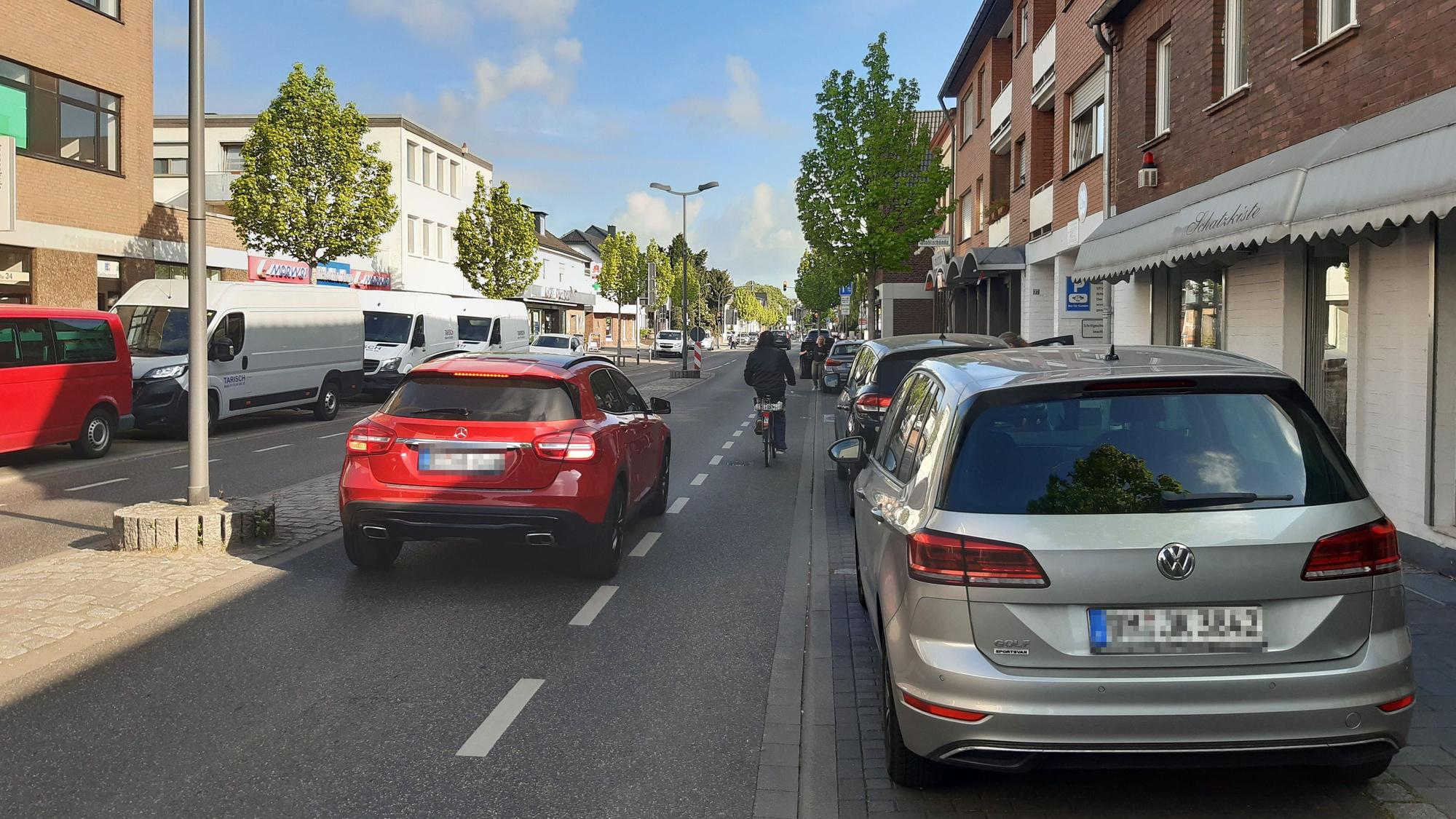 Das Foto zeigt einen Radfahrer, der vor einem Auto auf der Straße fährt.