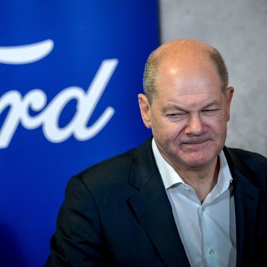 German Chancellor Olaf Scholz walks past the logo of US car giant Ford as he visits the company's plant in Cologne, western Germany, on December 10, 2024. In November 2024, Ford announced 4,000 more job cuts in Europe, mostly in Germany and Britain, in the latest blow to the continent's beleaguered car industry. (Photo by Sascha Schuermann / AFP)