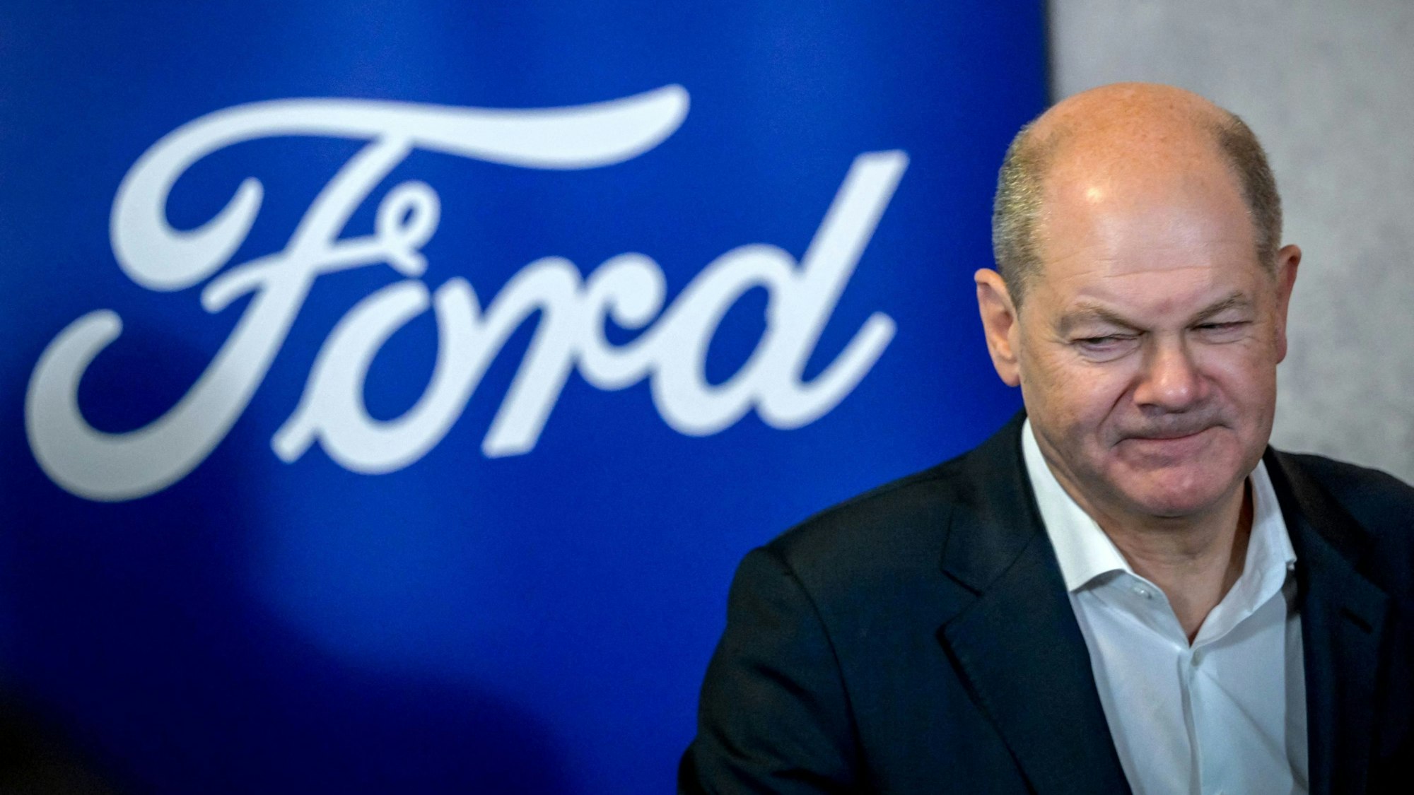 German Chancellor Olaf Scholz walks past the logo of US car giant Ford as he visits the company's plant in Cologne, western Germany, on December 10, 2024. In November 2024, Ford announced 4,000 more job cuts in Europe, mostly in Germany and Britain, in the latest blow to the continent's beleaguered car industry. (Photo by Sascha Schuermann / AFP)