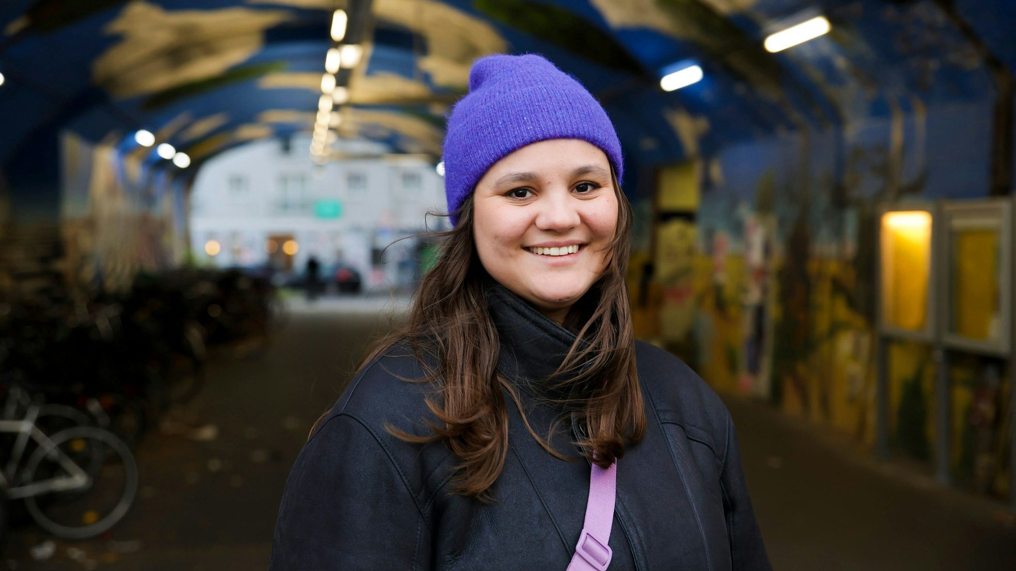 Eine Frau mit lila Mütze steht in einer Bahnhofsunterführung.