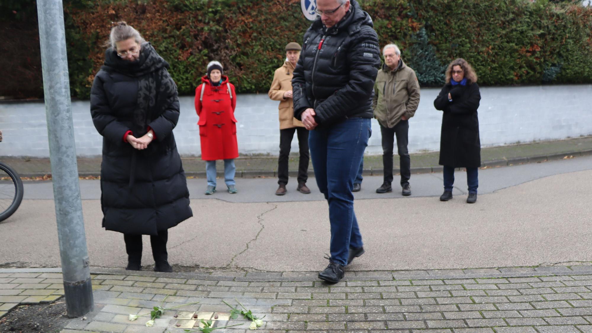 Menschen stehen auf einer Straße, in der goldene Stolpersteine verlegt wurden.