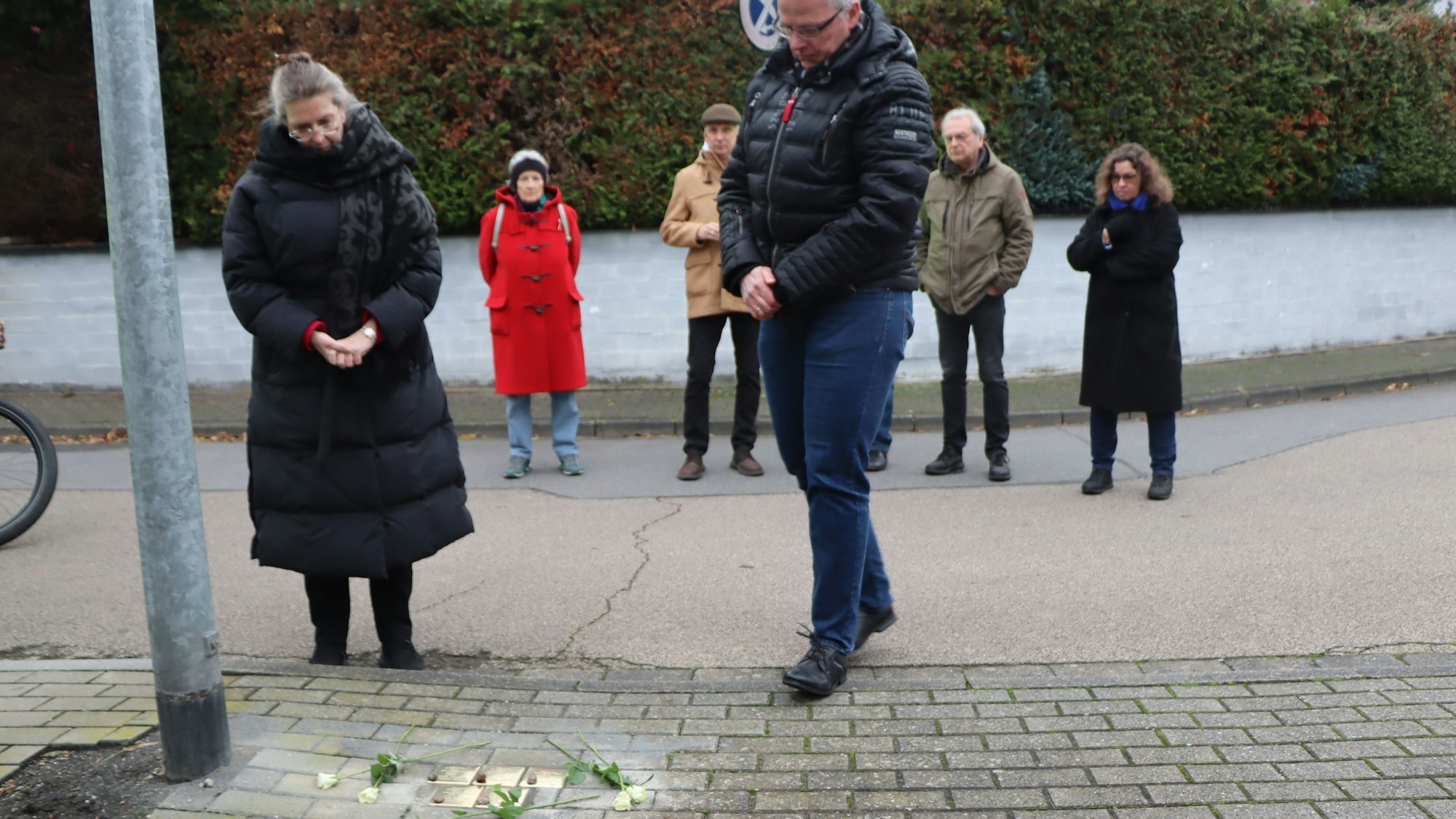 Menschen stehen auf einer Straße, in der goldene Stolpersteine verlegt wurden.