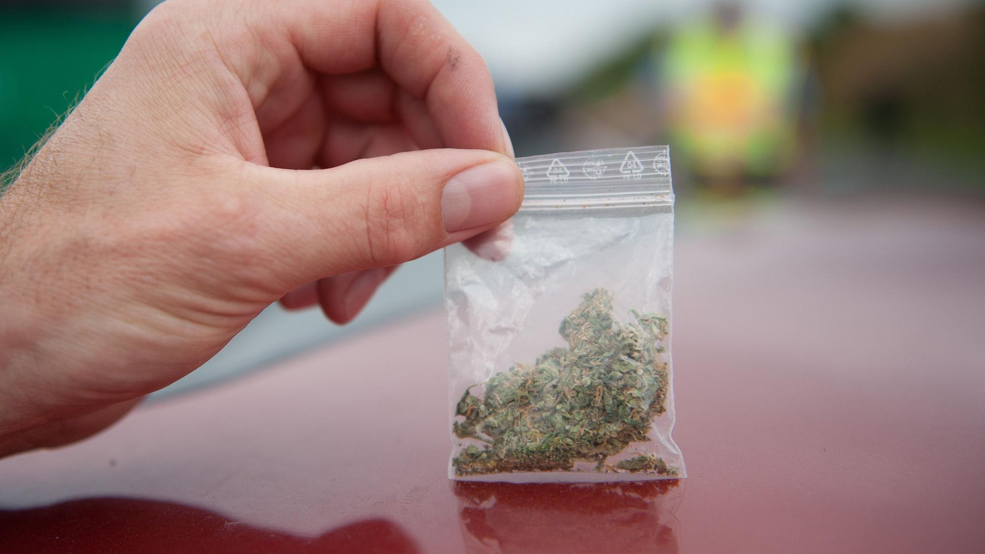 Ein Polizeibeamter hält ein Tütchen mit Cannabis hoch.