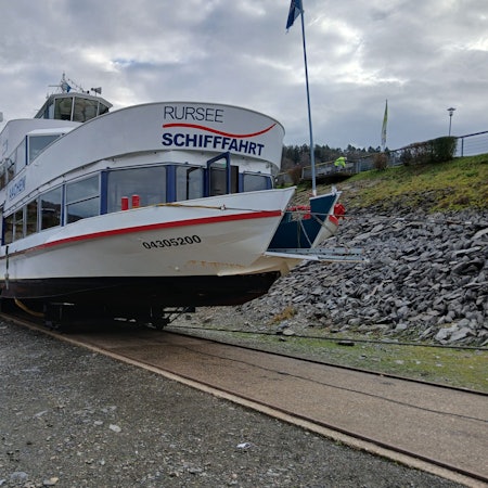 Die Mitarbeiter der Rurseeschifffahrt verfolgen, wie das weiße Schiff auf seinem Schlitten eine Rampe hinauf an Land gezogen wird.