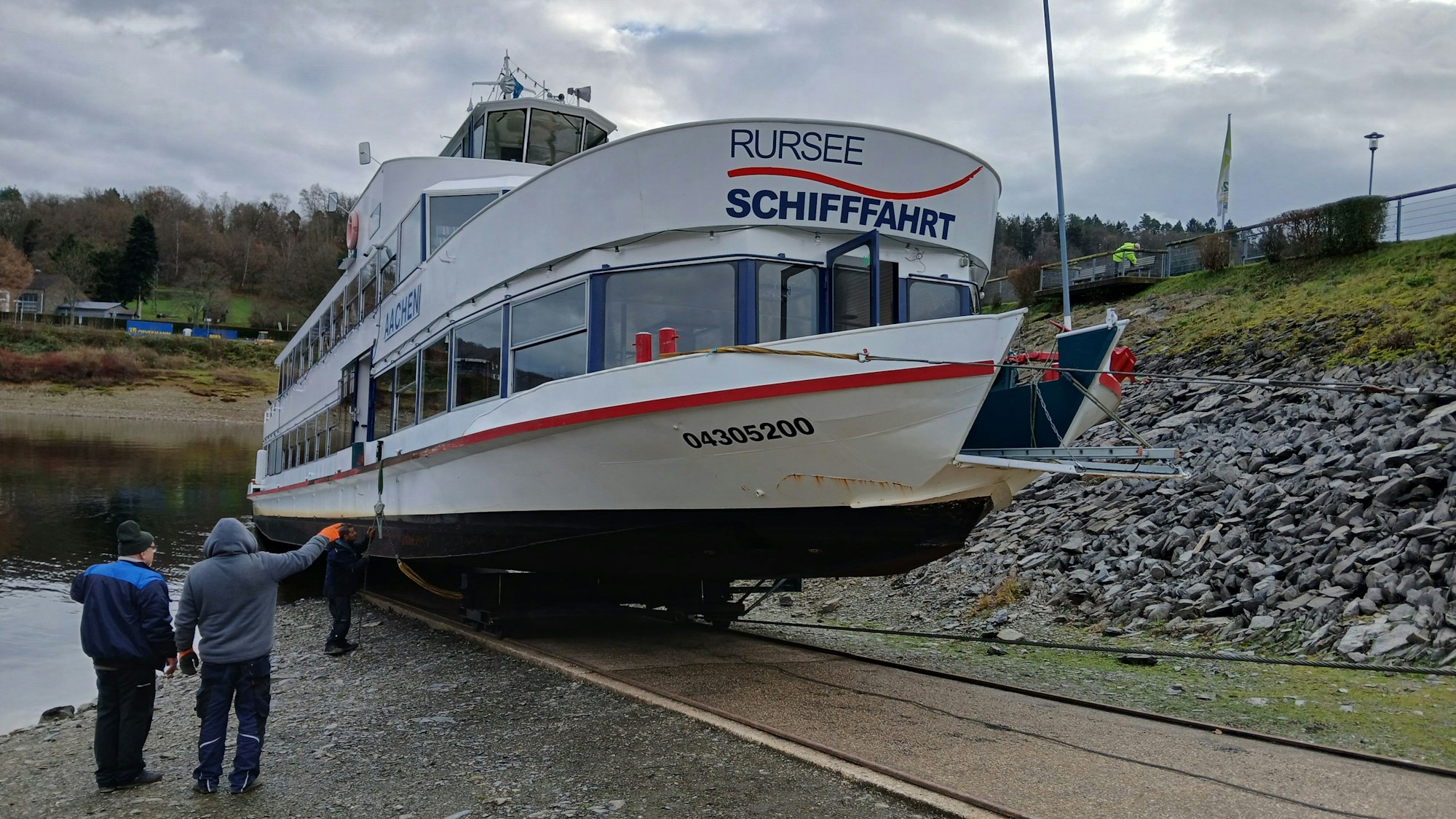 Die Mitarbeiter der Rurseeschifffahrt verfolgen, wie das weiße Schiff auf seinem Schlitten eine Rampe hinauf an Land gezogen wird.
