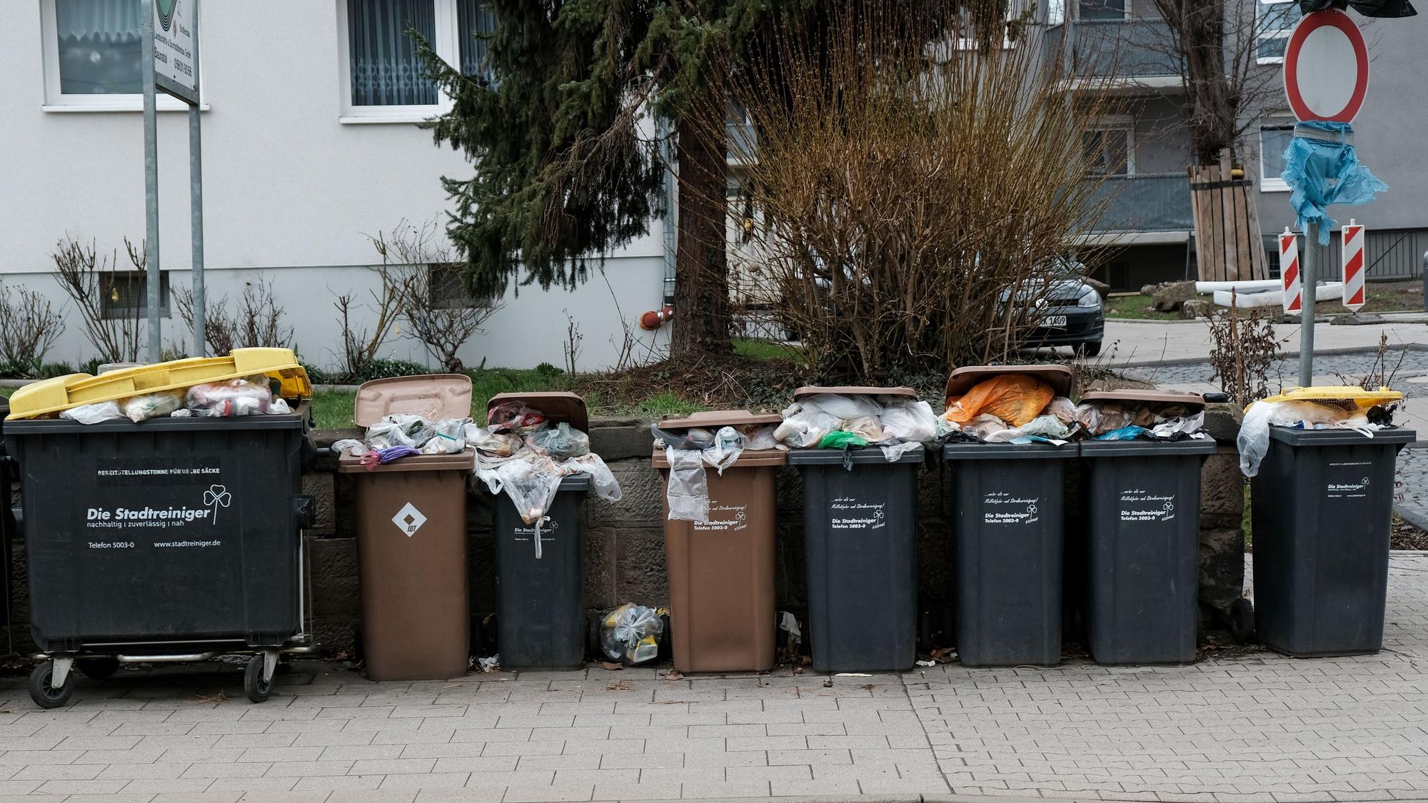 Mülltonnen vor einem Mietshaus an der Straße quillen über.