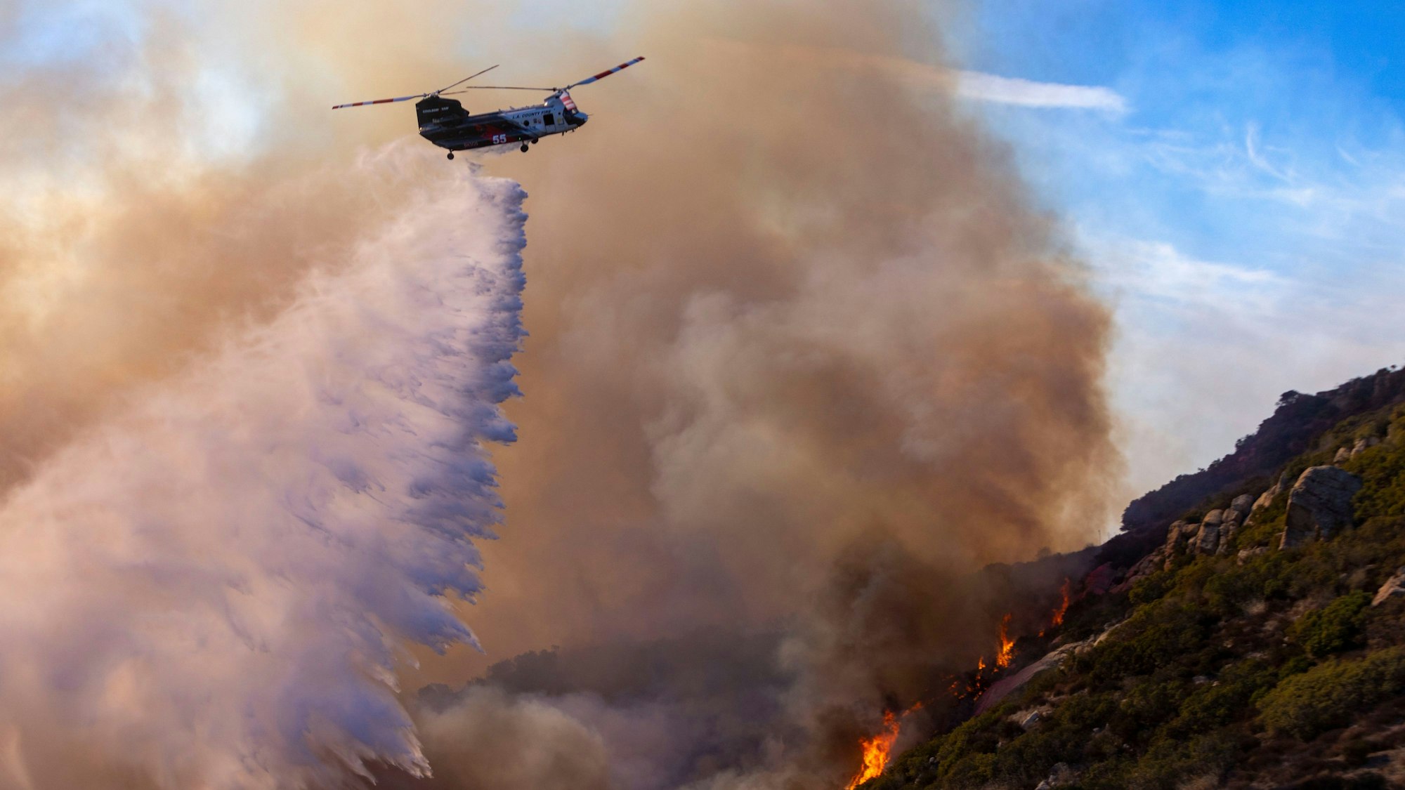 10.12.2024, USA, Malibu: Ein Löschhubschrauber des Los Angeles County wirft Wasser auf das Franklin Fire, um Häuser an der nahe gelegenen Costa Del Sol in Malibu zu schützen. Foto: Jill Connelly/ZUMA Press Wire/dpa +++ dpa-Bildfunk +++