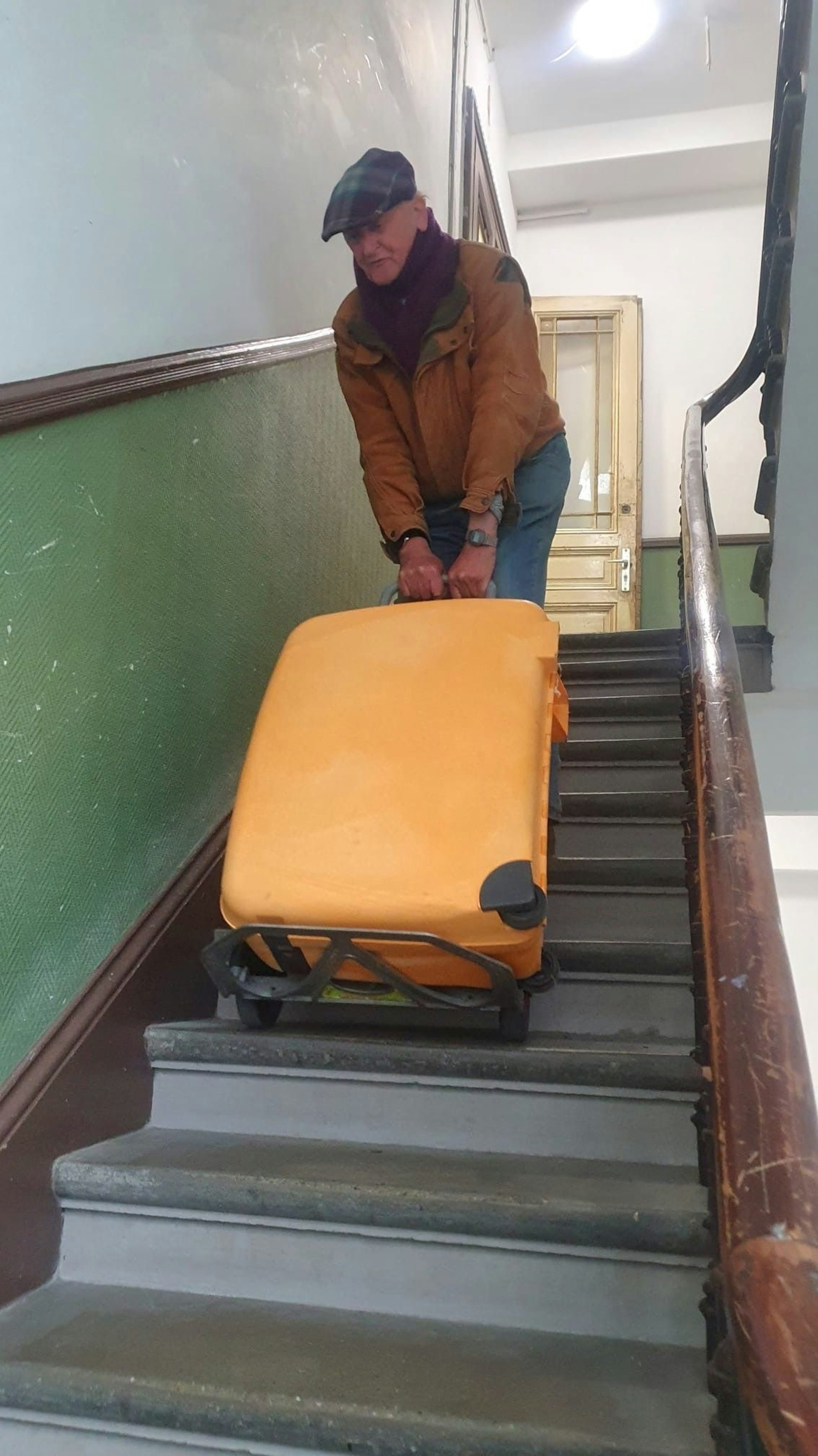 Klaus J. zieht einen großen Koffer über die Treppen seines Treppenhauses.