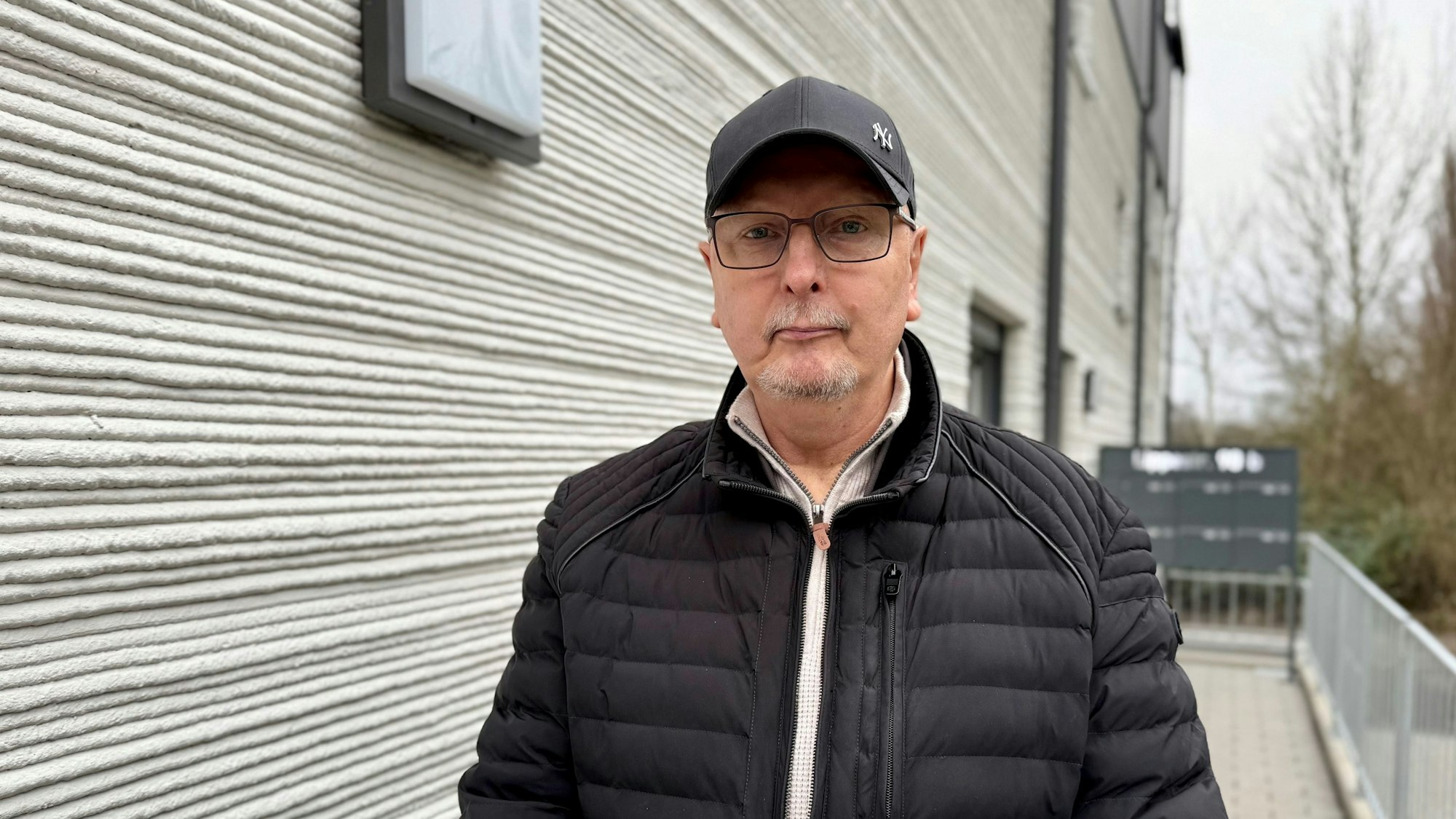 Peter Woryna steht im Eingangsbereich des Mehrfamilienhauses, im Hintergrund ist die geschichtete Fassade des Neubaus zu sehen.