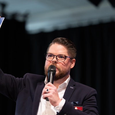 Ein Mann hält einen europäischen Pass und ein Mikrofon in der Hand.