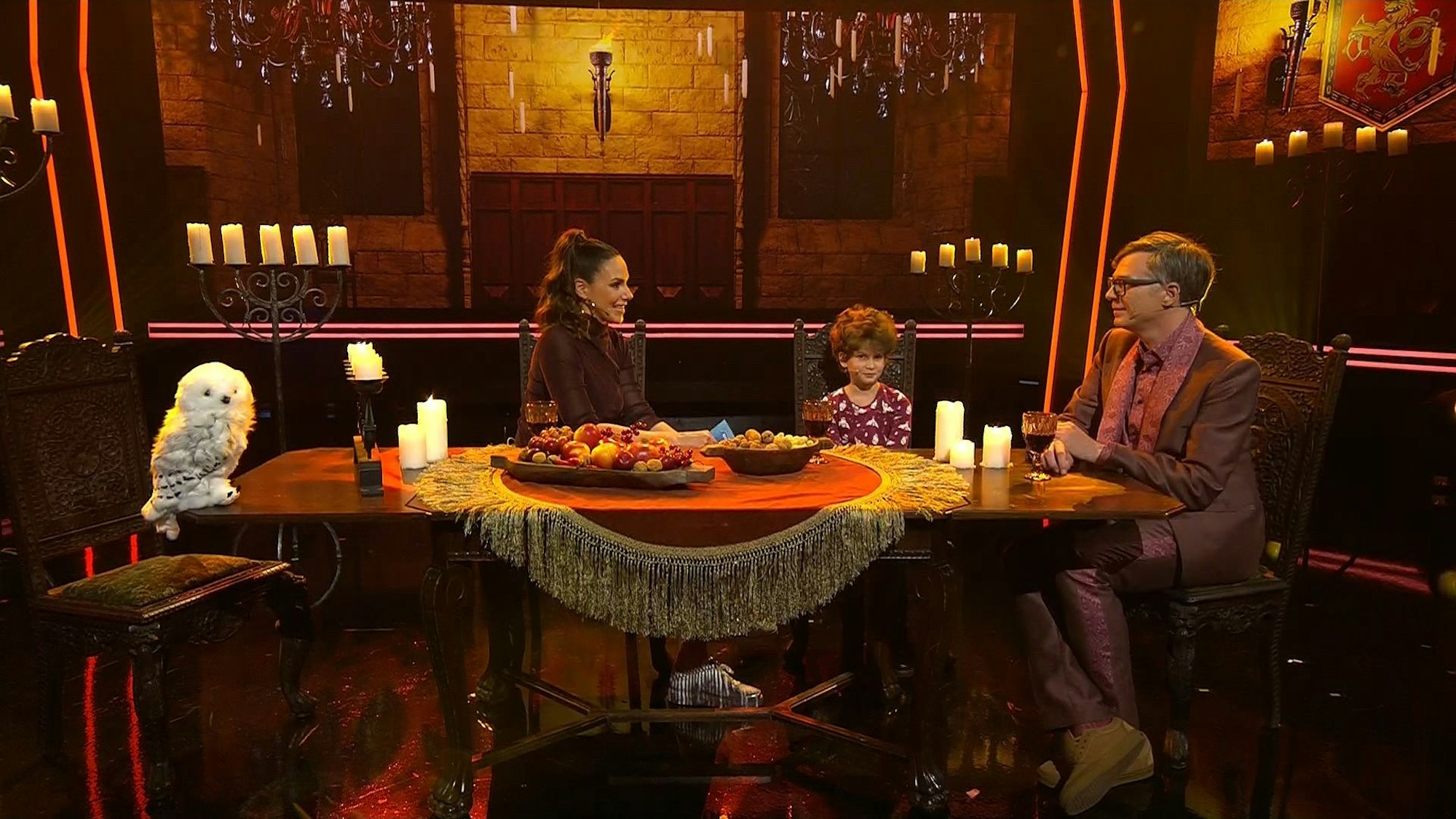 Eine Frau, ein Mädchen und ein Mann sitzen an einem Tisch in einem Fernsehstudio.